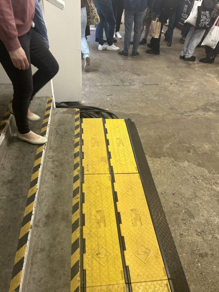 A yellow wheelchair ramp is installed alongside stairs in an indoor setting. Several people are visible in the background.