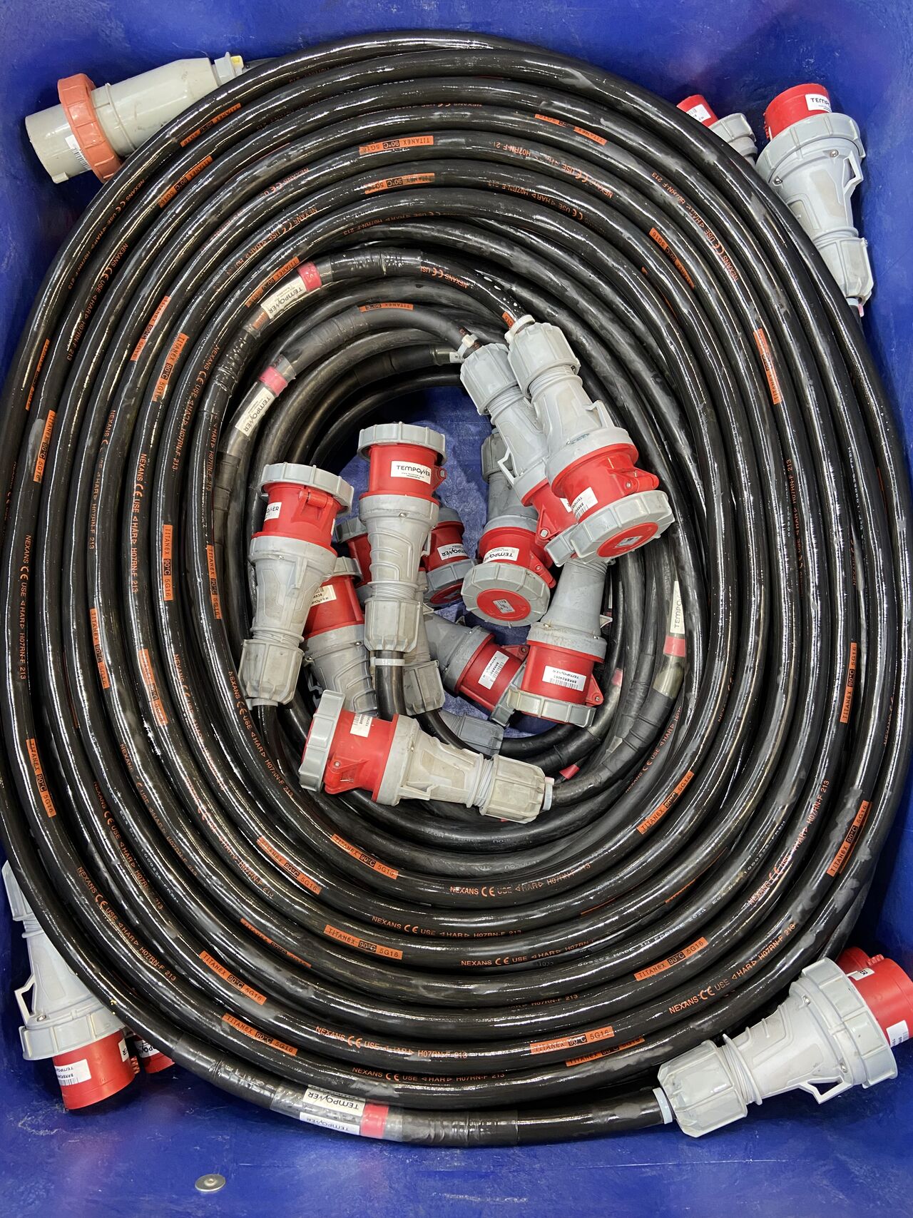 Coiled black industrial cables with red and gray connectors are stacked together in a blue container.